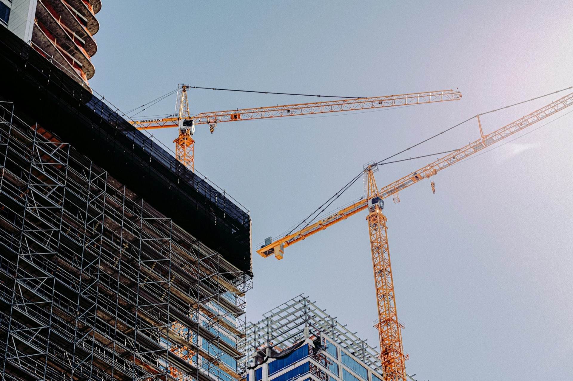 Tower cranes beside a commercial building wrapped in scaffolding